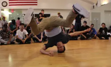 A man is demonstrating a breakdance move with participants watching from the side