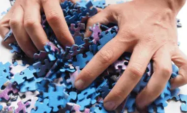 two hands grab a pile of blue and purple puzzle pieces