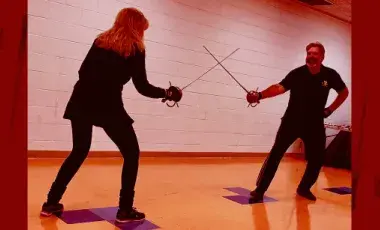 A woman and a man in a fighting stance while crossing swords.