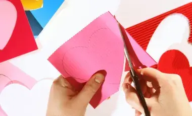 Hands using scissors to cut out heart shapes from textured paper.