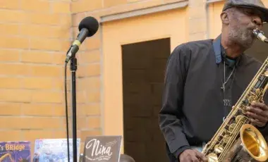 Man with a black shirt and hat, holding a gold saxophone
