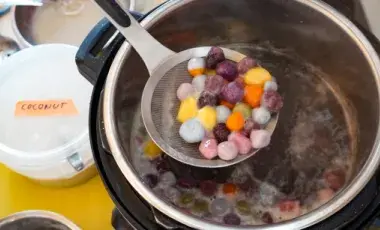 A ladle full of colorful dumplings over a large pot of dumplings.