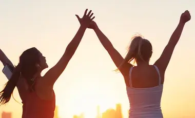Two women exercising outside with arms raised. 