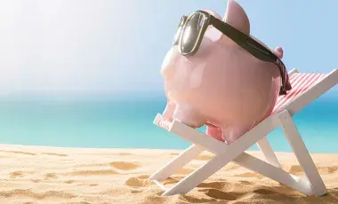 A relaxing, pink piggy bank wearing sunglasses sitting on a beach chair at the beach