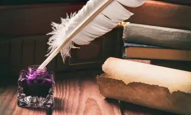 Old inkstand with feather near scroll and books