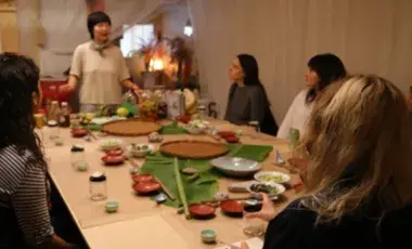 Picture of Jessica Wang giving a food preparation demo to people seated around a table.