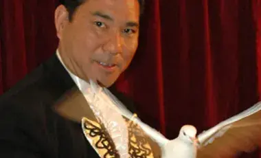 A magician holds a dove with wings outstretched.