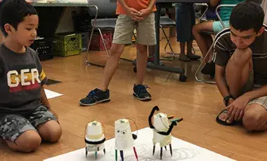 Children watch as their Art Bots bounce around on marker legs, making their own "art".