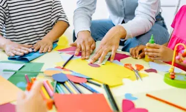Children and an adult gather around a table and create art using a variety of materials. 