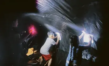 Two kids holding paper up to the sides of the black plastic wall of the planetarium while an adult shines a flashlight so they can see