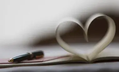 A black pen rests on an open book with pages folded to resemble a heart shape