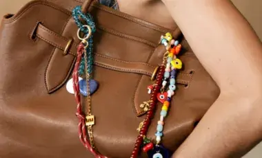 In the picture is a woman's hand holding a tote bag decorated with bead bag charms