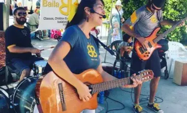 Performer Isabel Brazon playing guitar with band outdoors.