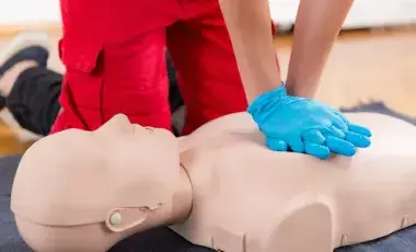 image of a person wearing blue gloves performing hands-only CPR on a mannequin