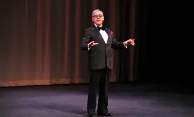 A performer holds the signature cigar, and wears the tuxedo and glasses of famed comedian George Burns