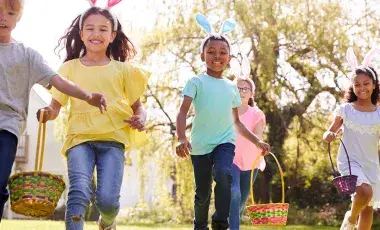 Group of children wearing bunny ears running to pick up Easter eggs during Easter egg hunt.