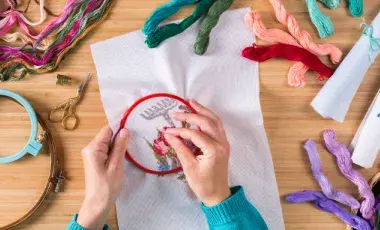 A pair of hands stitching on an embroidery hoop.
