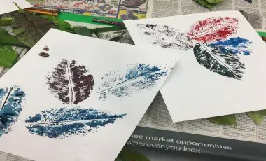 Pieces of paper with colorful images of leaves, actual leaves, and crayons, on top of pieces of newspaper