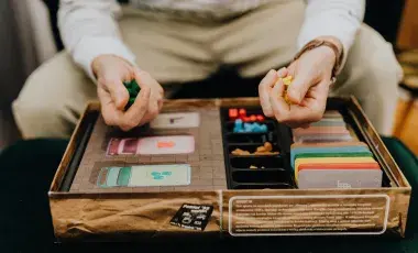 Person holding game pieces over a game board as if about to roll a turn.