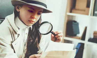 Girl in a trench coat and fedora looking through a magnifying glass