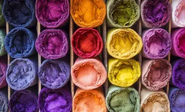An assortment of tightly rolled fabric bolts in a vibrant spectrum of colors.