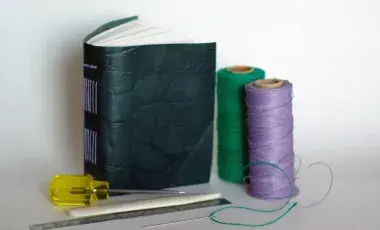 small book with a leather cover next to two spools of thread and other tools