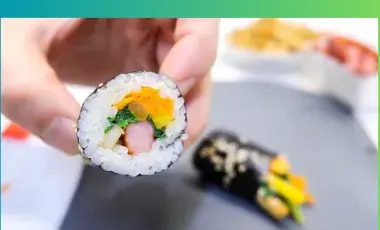 A hand grabbing a slice of mini kimbap and a out of focus roll in the background