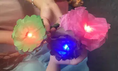 Close-up of children's hands showing the camera their lit-up tissue paper flowers in colors green, blue and pink.