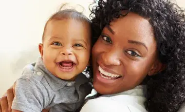 Baby and caregiver smile at the camera. 