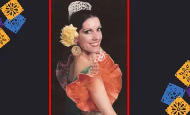 A woman in a dance costume surrounded by papel picado. 