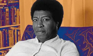 Author Octavia E. Butler sitting on a chair in front of a bookshelf