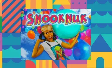 ​​A colorful geometrical background borders an image of the performer, Snooknuk, holding a huge bouncy ball over her shoulders as a cascade of multi-colored balloons floats behind her. 