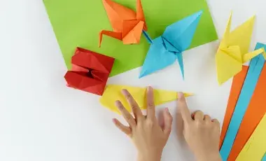 Child's hands folding paper into different shapes