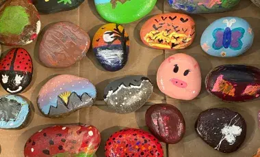 Colorfully painted rocks featuring animals, sunsets, butterflies, and abstract designs displayed on a table.