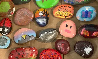 A collection of painted rocks featuring various colorful designs, including animals, landscapes, patterns, and abstract art, displayed on a flat surface.