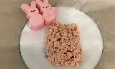 A pink Rice Krispies treat and two pink Bunny Peeps on waxed paper on a plate