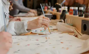 a woman is painting on a tote bag