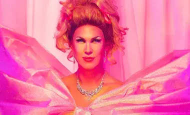 Head and shoulders view of Drag Performer Pickle in a pink gown, with a jeweled necklace and earrings, big hair, and full make-up.