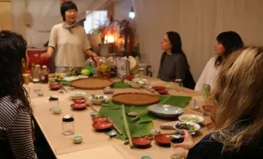 Chef Jess Wang teaching a cooking class to a table full of patrons. 