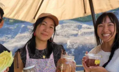 3 people are pictured holding jars of pickles under an umbrella