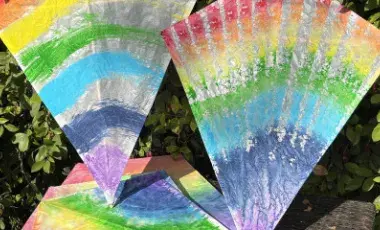 A pile of rainbow-painted kites against a leafy background.