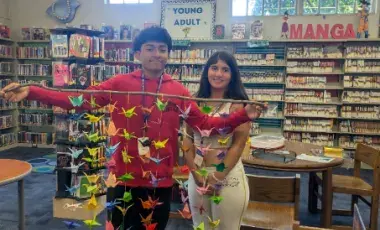Two teens holding a stick with paper cranes