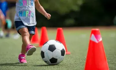 A child kicking a soccer ball between orange cones