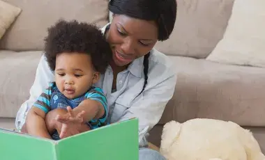 A woman holds a toddler in her lap while they read a book together