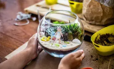 Two hands holding a glass terrarium with a beach scene inside