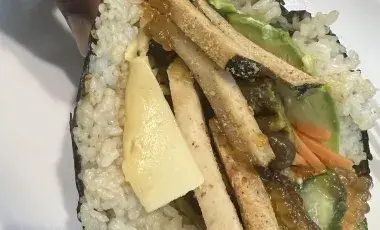 Vegan sushi taco being held over a white plate.