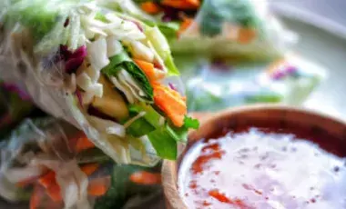 Image of two spring rolls with fresh veggies and a red dipping sauce