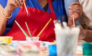 colorful paints and paintbrushes on table with people in background