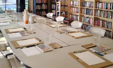 Room prepared for an art program with boards, papers, watercolors and a still life with three vases in the center