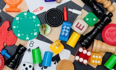 Assorted board game pieces, cards, and dice are scattered on a checkered surface.